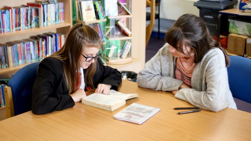 student reading a book in South Wirral high school library
