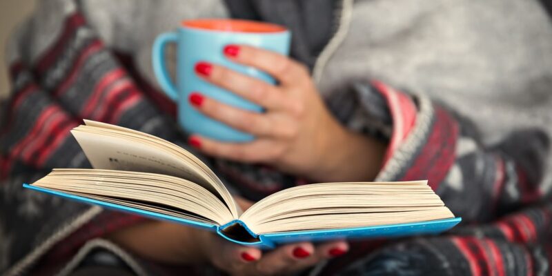 a close up of a woman reading a book up a mug and lots of blankets